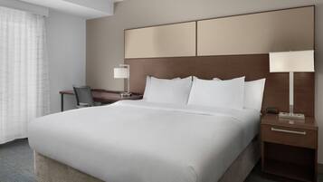 A hotel room with a large bed, a bedside table with a lamp, a chair, and a desk.