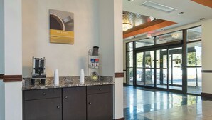 A reception area with a coffee machine, a trash can, and a glass door leading outside. - Motel 6 Decatur, GA (Decatur)