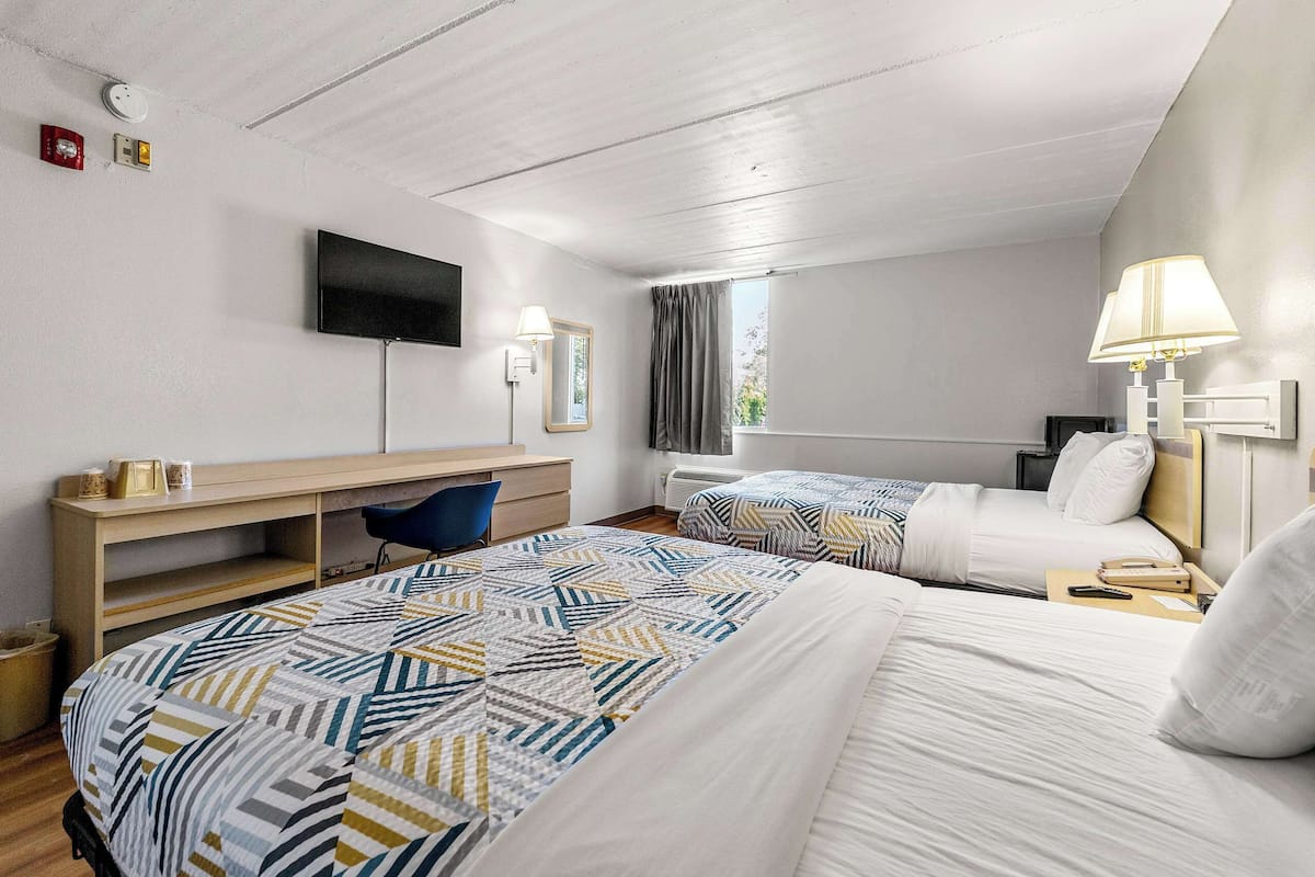 A hotel room with two beds, a desk, a TV, and a window with curtains.