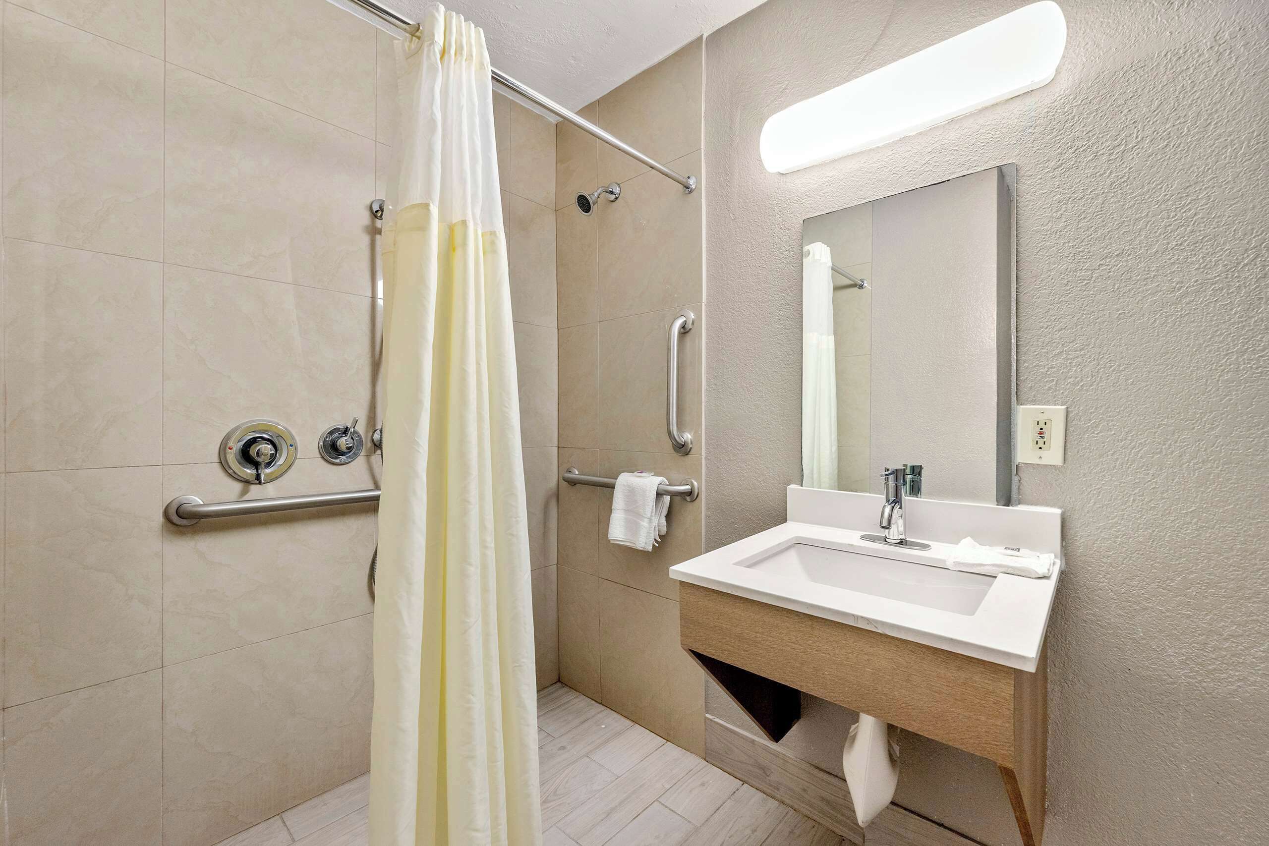 A modern bathroom with a shower, grab bars, a sink, and a mirror.