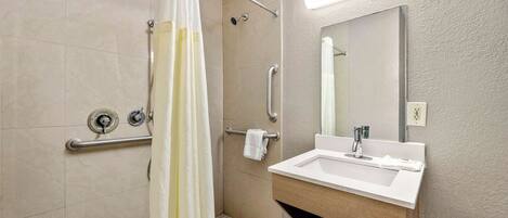A modern bathroom with a shower, grab bars, a sink, and a mirror.
