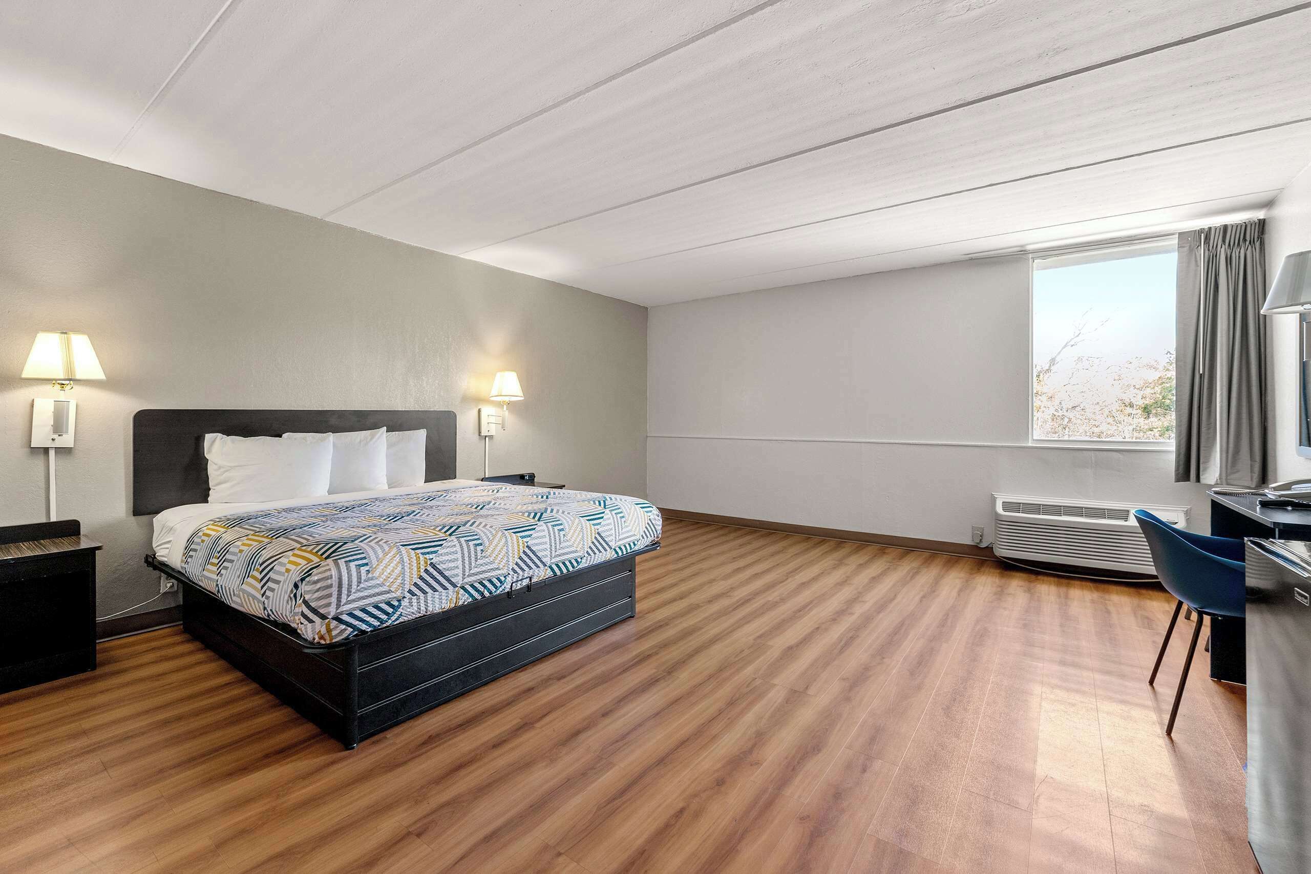 Une chambre d’hôtel avec un lit, deux lampes de chevet, un bureau avec une chaise et une grande fenêtre.
