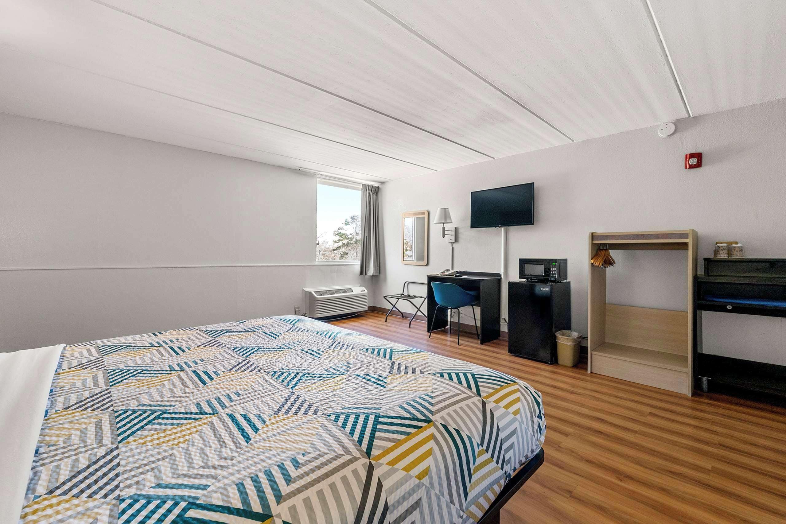 A hotel room with a bed, a desk, a chair, a TV, and a small kitchenette.