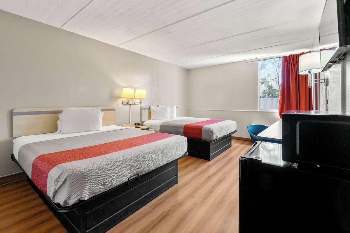 A hotel room with two beds, a desk, a TV, and a window with curtains.