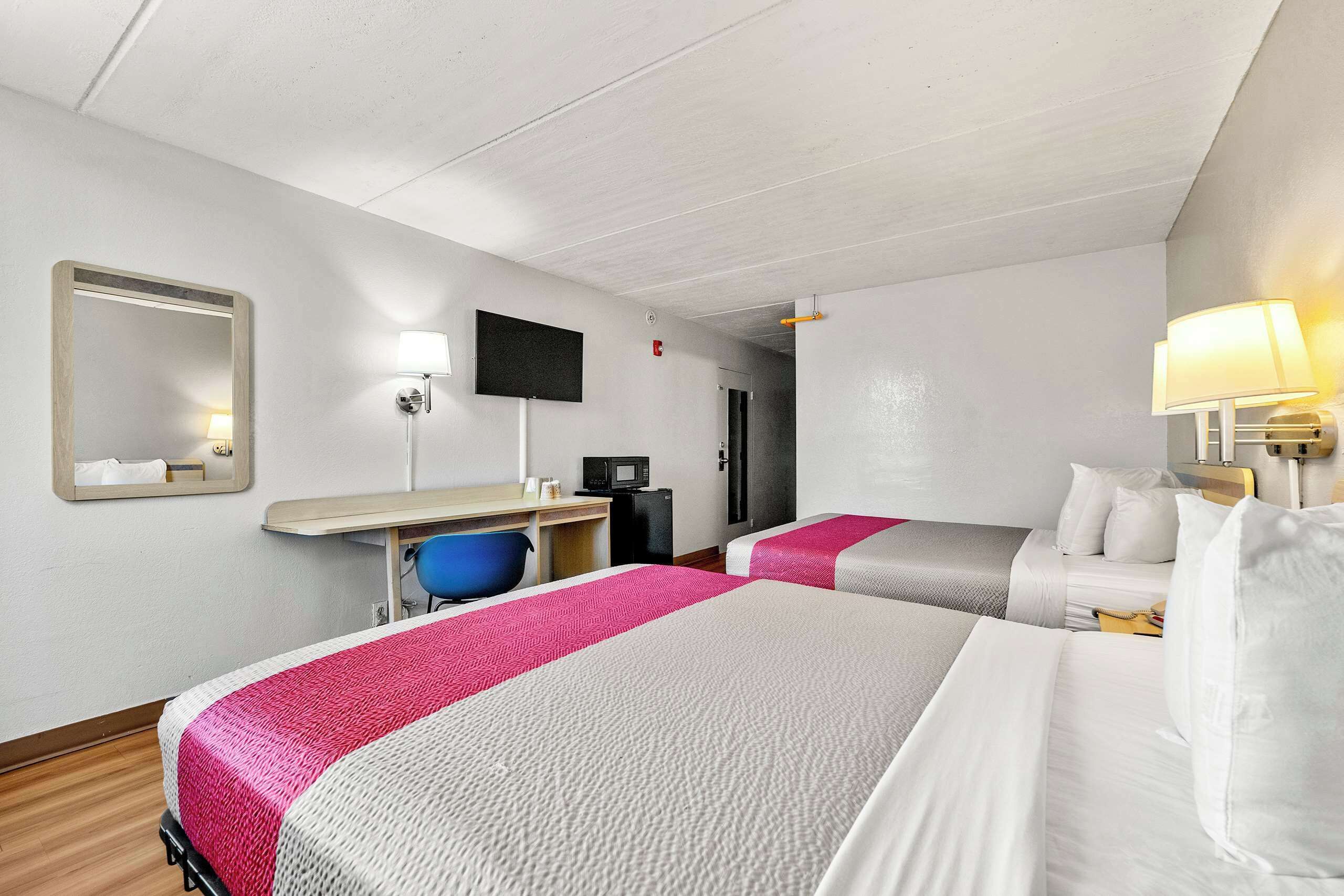 A hotel room with two beds, a desk, a chair, a TV, and a mirror.