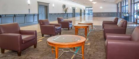 Een ruime lobby met leren fauteuils, een salontafel met glazen blad en een vloerbedekking.