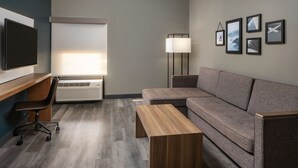 Quarto moderno com sofá cinzento, mesa de centro de madeira, escrivaninha com cadeira, abajur de chão e quadros nas paredes.