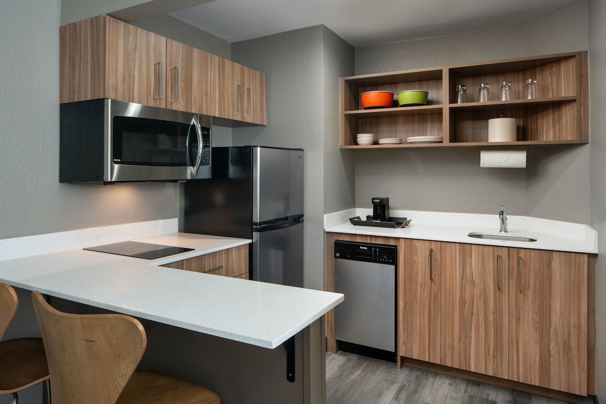 A modern kitchen with wooden cabinets, stainless steel appliances, and a white countertop.