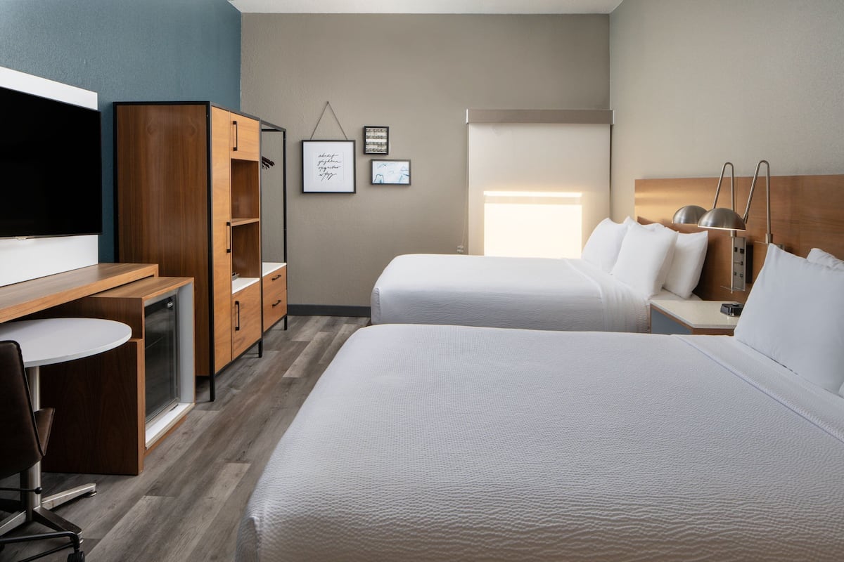 A hotel room with two beds, a desk with a chair, a television, and a wardrobe.