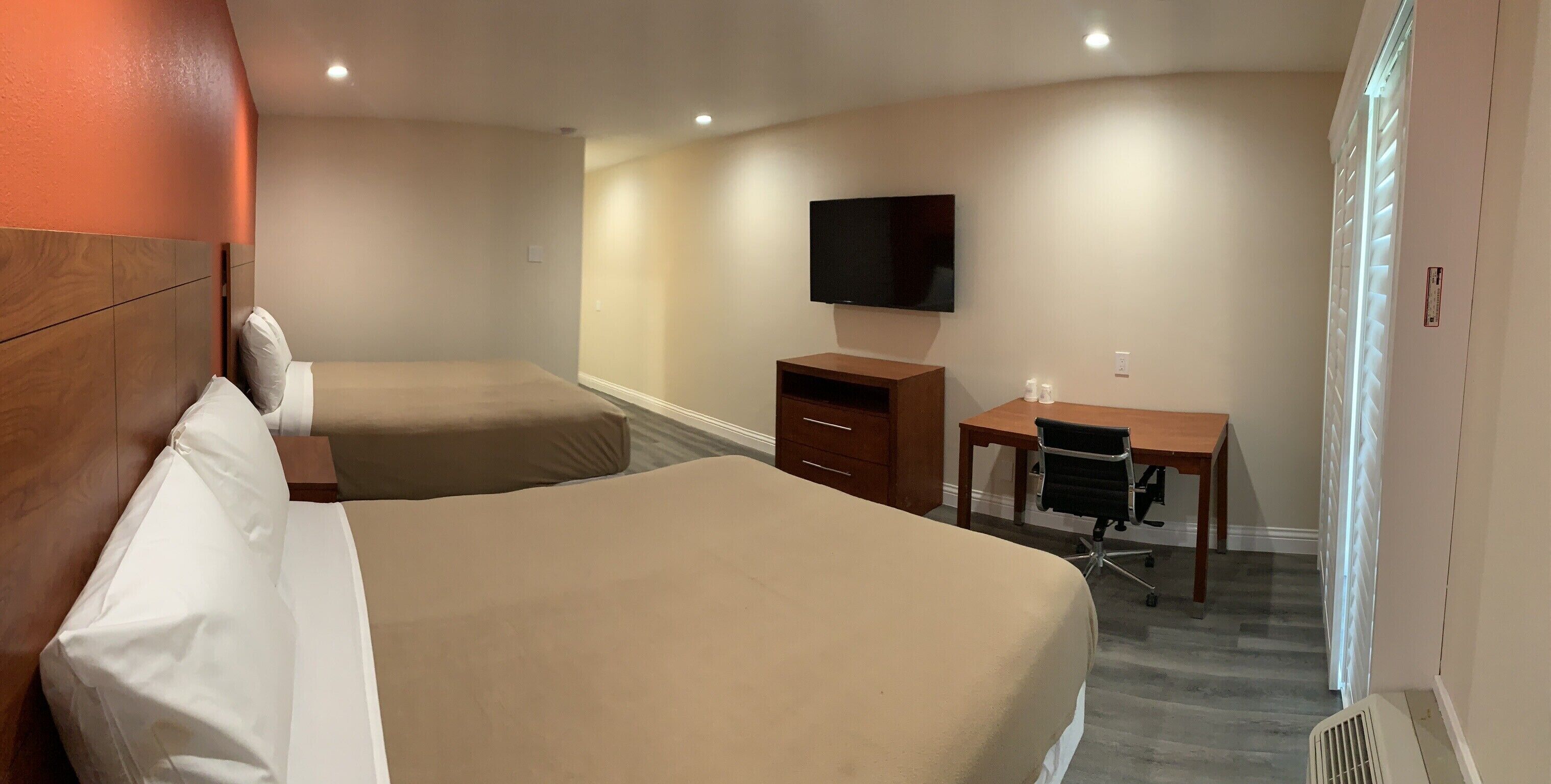 Una habitación de hotel con dos camas, un escritorio, una silla, un televisor y una ventana con persianas.