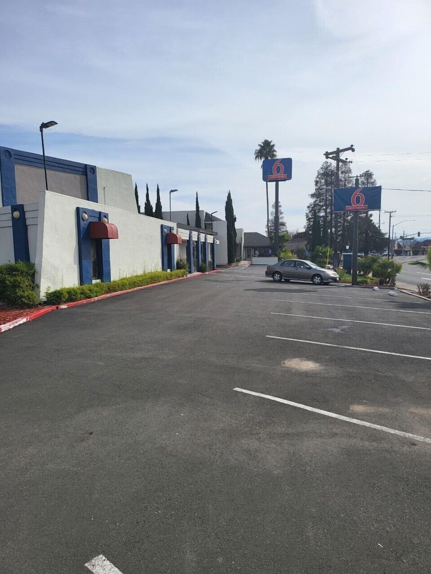 A parking lot with a building featuring a blue and white facade, a red awning, and a sign with the number 6.