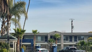 A parking lot with two cars, a building with balconies, and palm trees. - Motel 6 Vallejo, CA – Napa Valley (Vallejo)