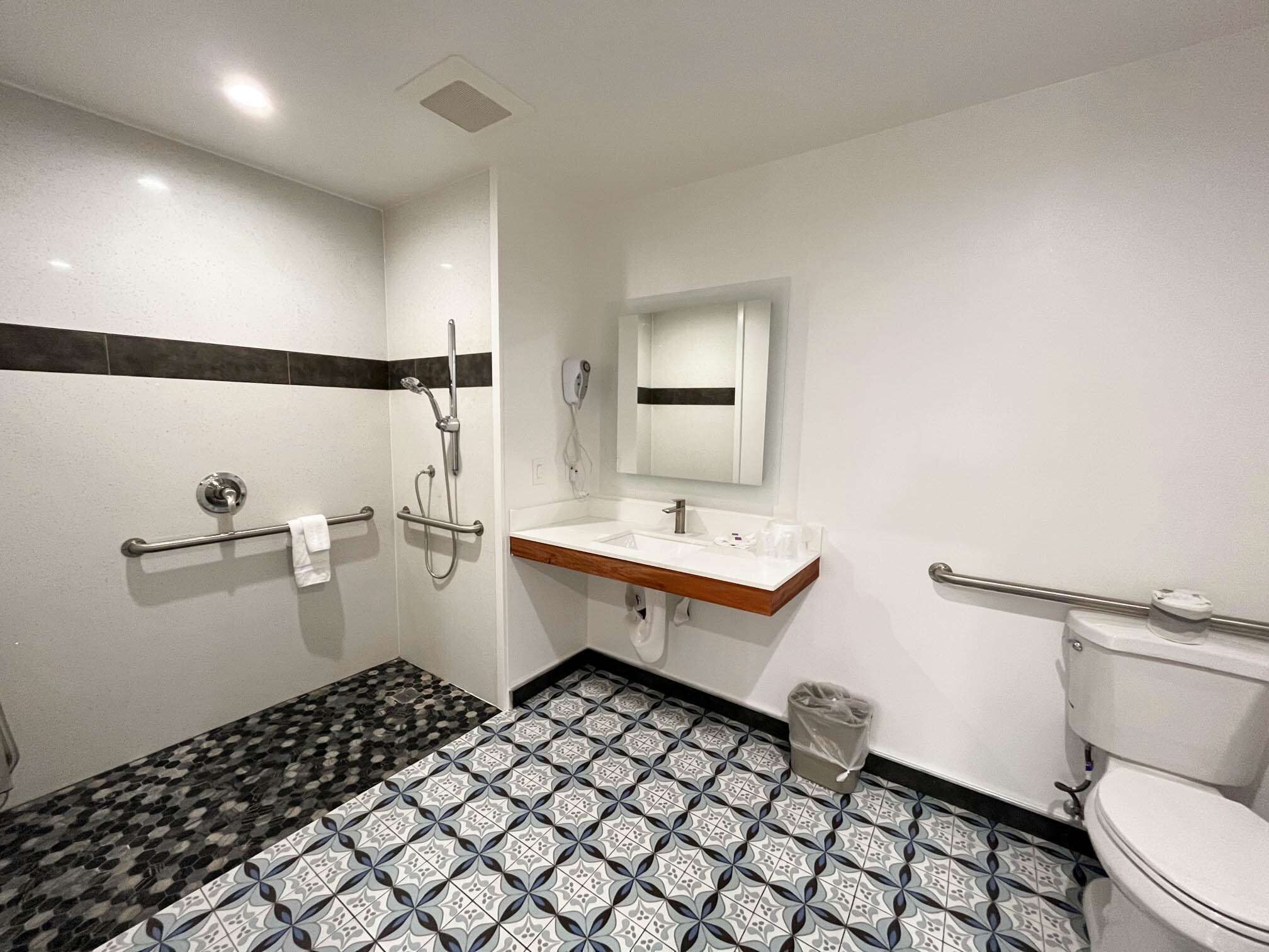 A bathroom with a shower, toilet, sink, and a mirror.