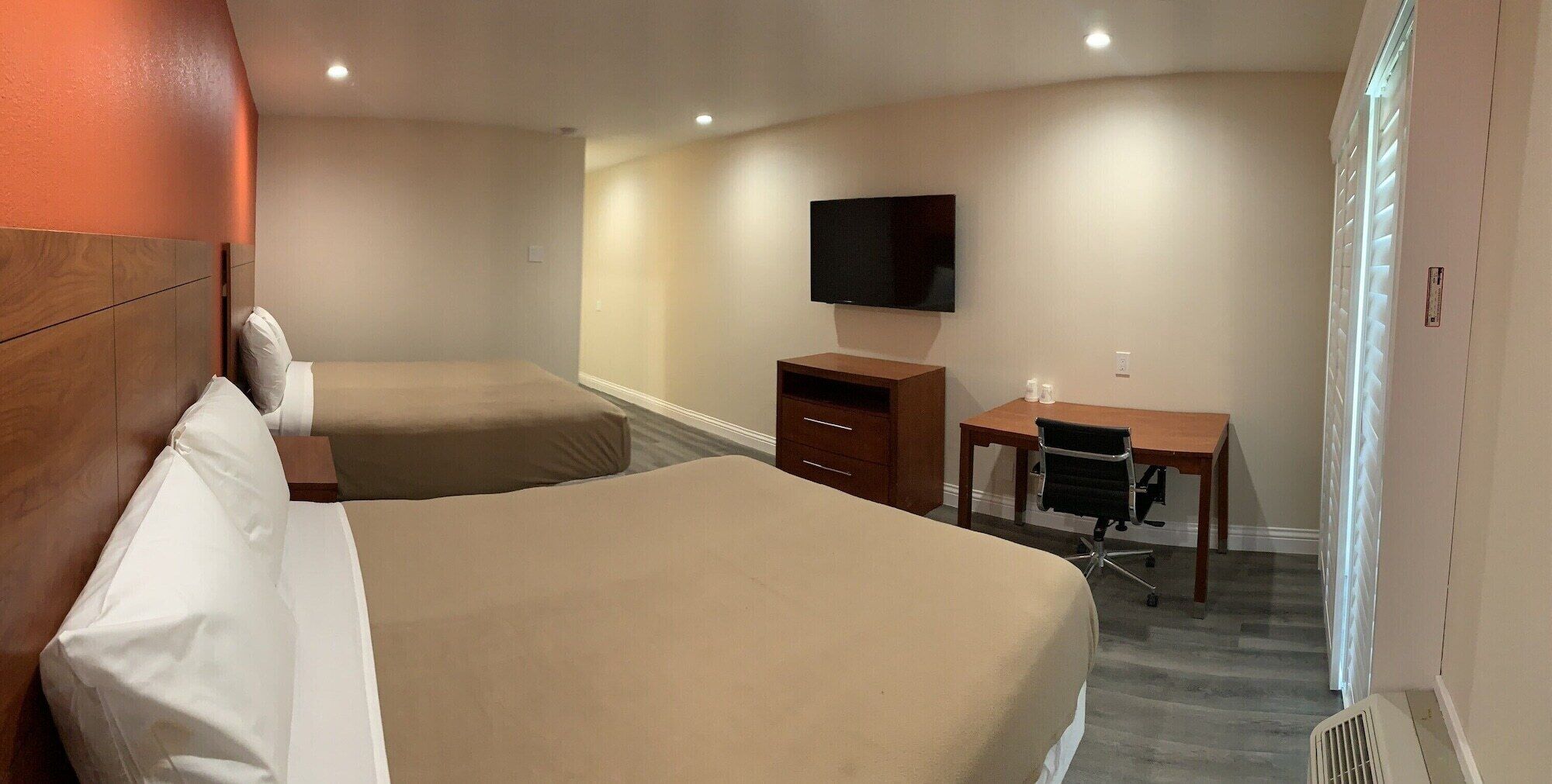 A hotel room with two beds, a desk, a chair, a television, and a window with blinds.