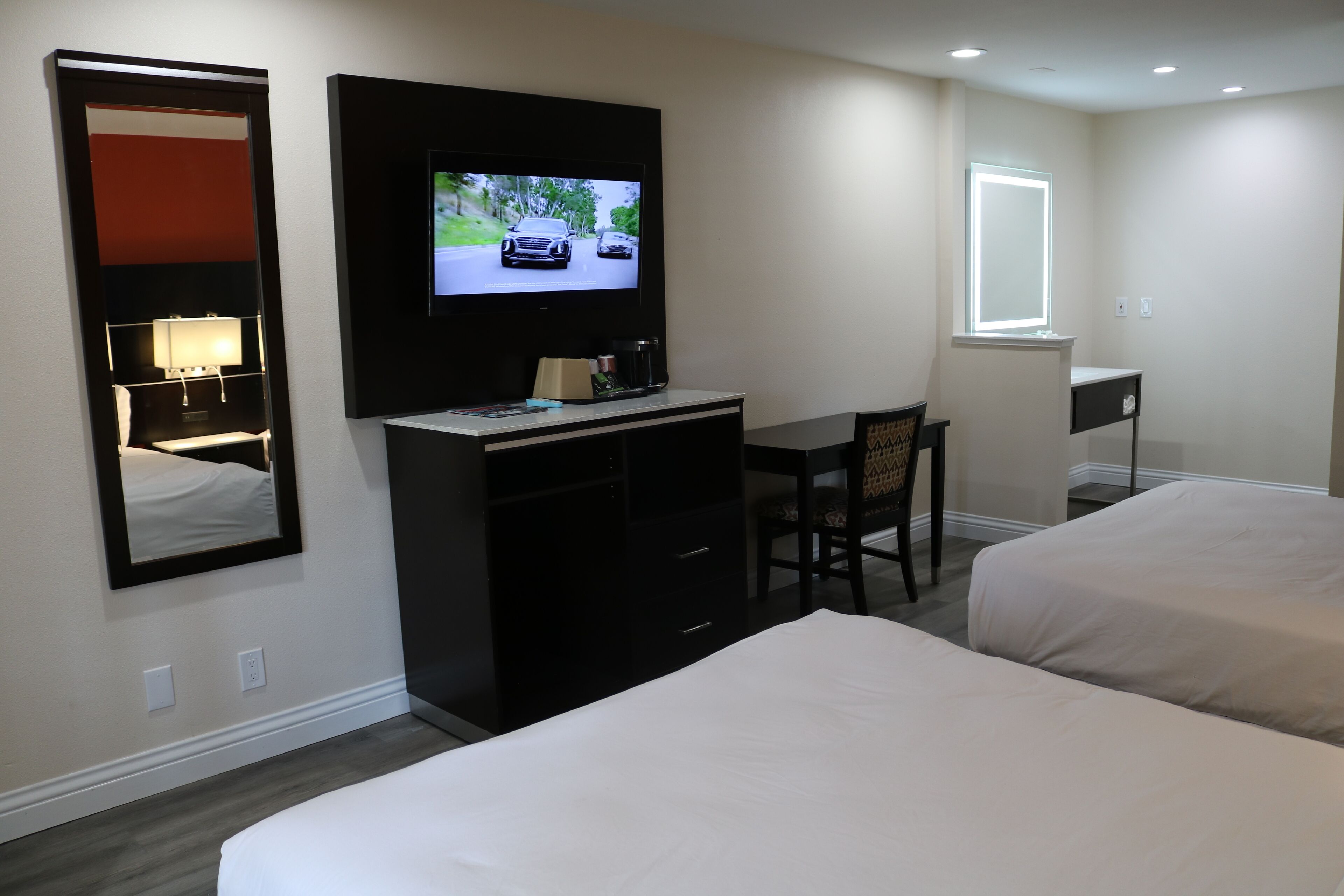 Habitación de hotel con dos camas, un escritorio, un televisor, un espejo y una ventana.