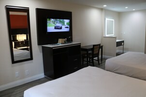 Habitación de hotel con dos camas, un escritorio, un televisor, un espejo y una ventana.