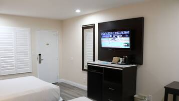 Habitación de hotel con dos camas, un televisor montado en la pared, un escritorio con silla y un cubo de basura.