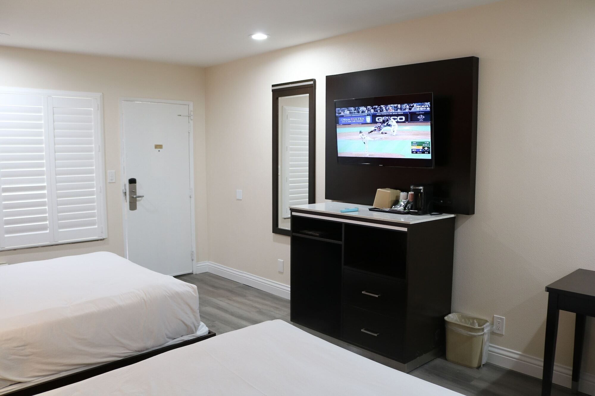 A hotel room with two beds, a TV mounted on a dark cabinet, a small trash bin, and a white door.