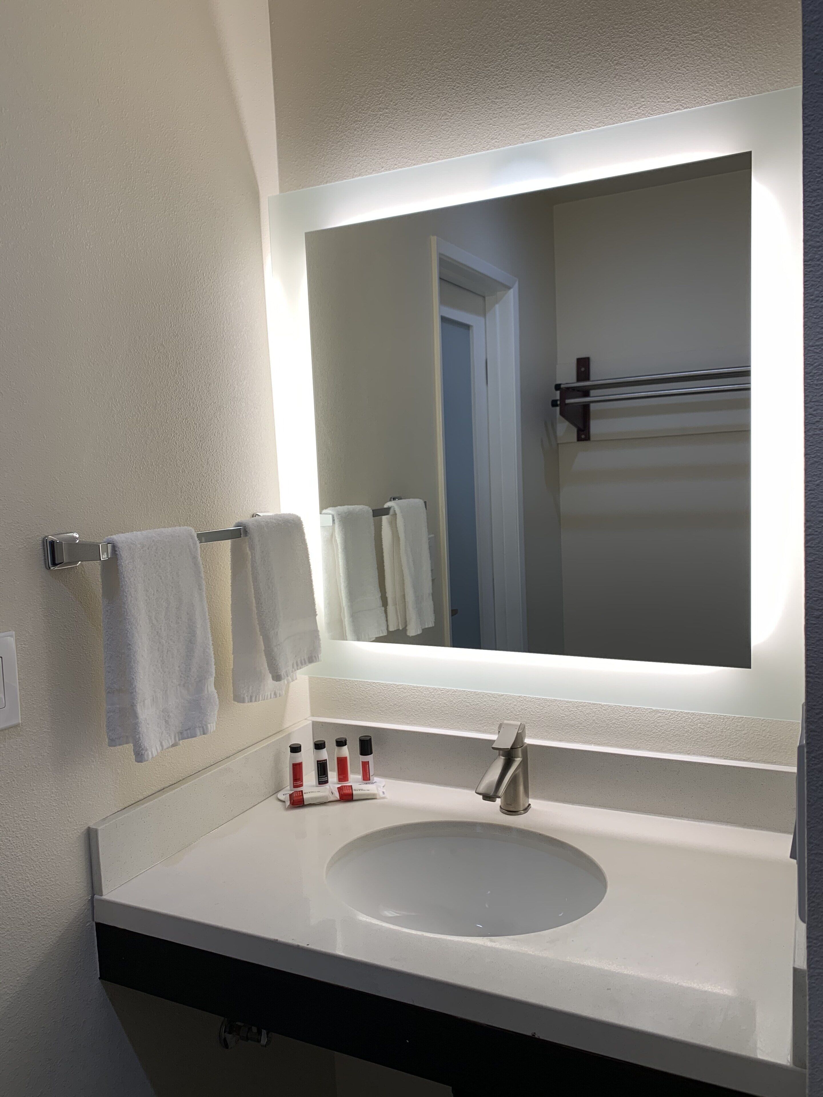 A bathroom with a white sink, a large mirror, and two towels hanging on a towel rack.