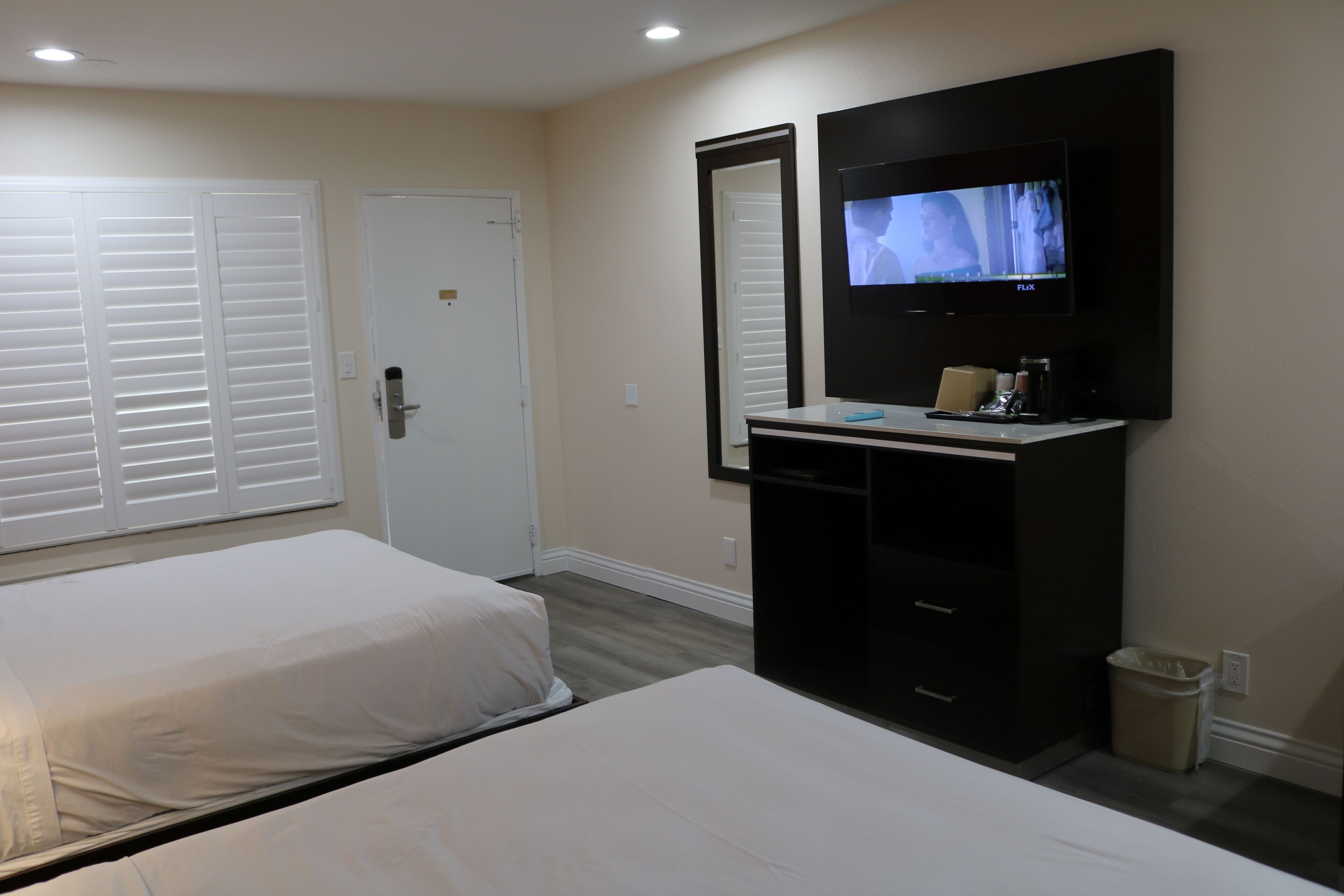 A hotel room with two beds, a TV, a desk with a chair, and a trash bin.