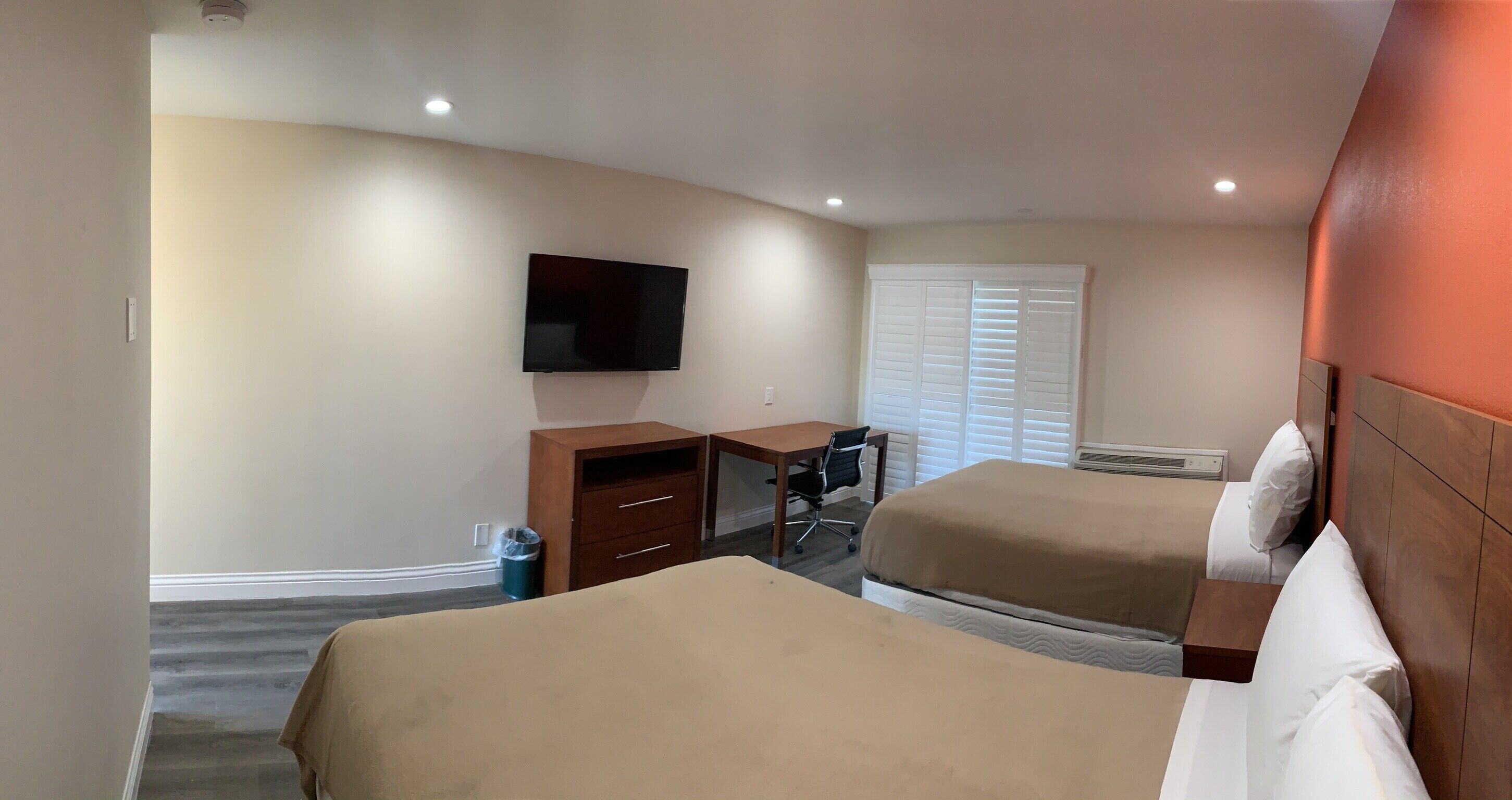 Habitación de hotel con dos camas, un escritorio, una silla, un televisor y una ventana con persianas.