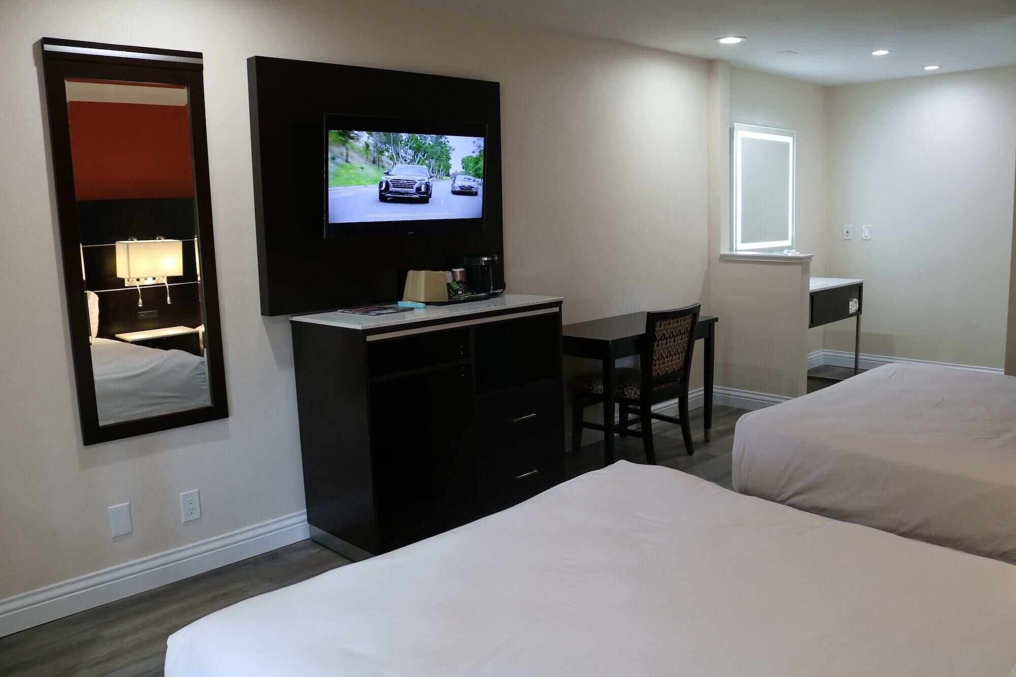 A hotel room with two beds, a desk, a TV mounted on the wall, a mirror, and a window.