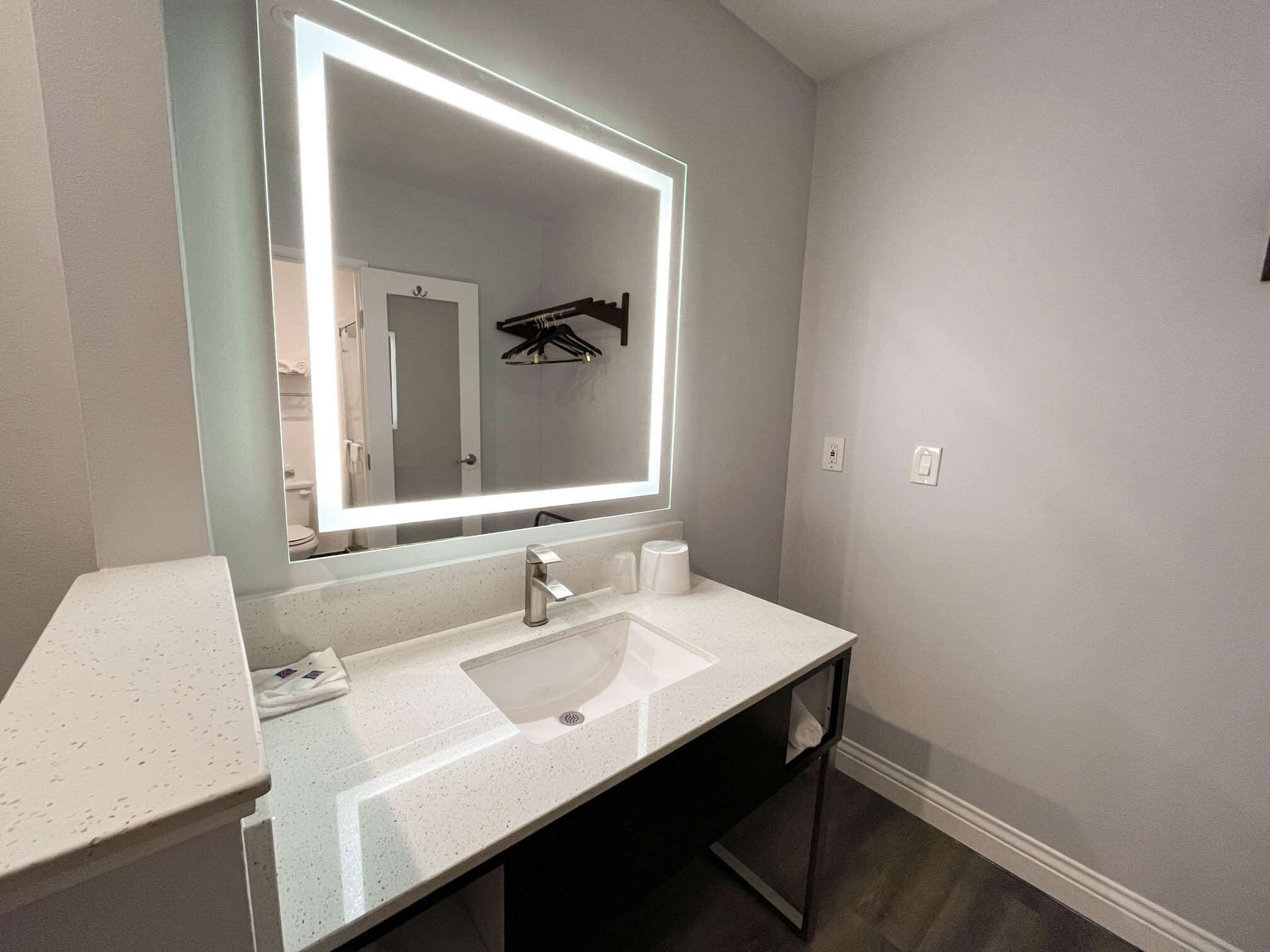 A modern bathroom with a large mirror, a white sink, and a dark wooden vanity.