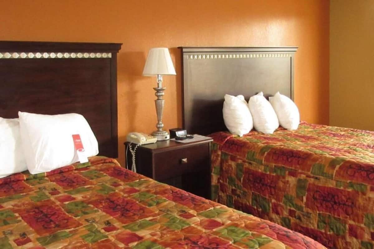 Habitación de hotel con dos camas, una mesita de noche con lámpara, teléfono y una etiqueta roja en el cojín.