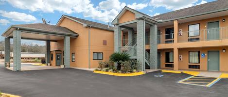 Un motel con zona de estacionamiento techada, una escalera al nivel superior y un espacio reservado para personas con discapacidad.