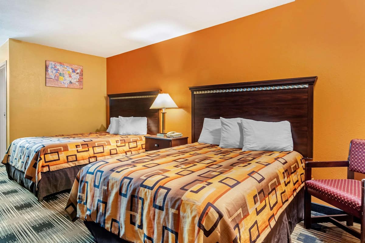Una habitación de hotel con dos camas, una mesita de noche, una silla y una lámpara de pared.