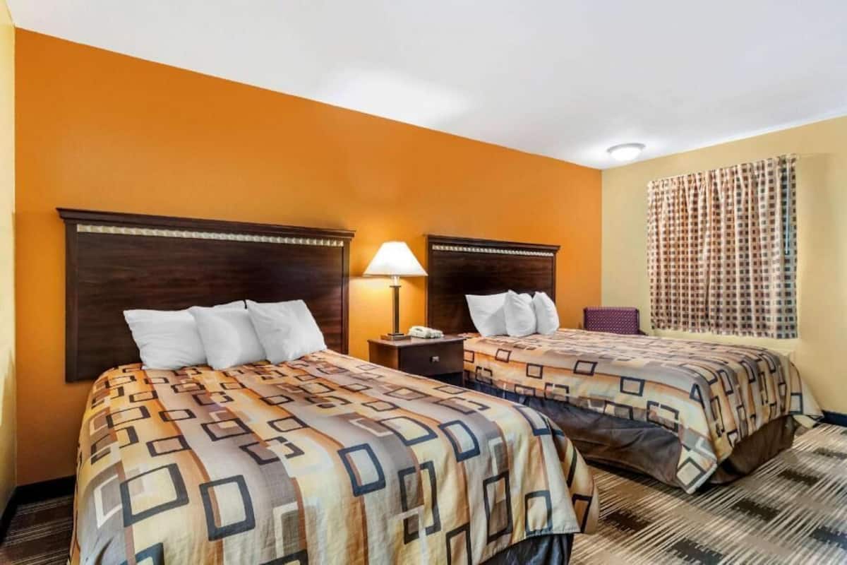 Habitación de hotel con dos camas, una mesita de noche, una lámpara y una ventana con cortinas.