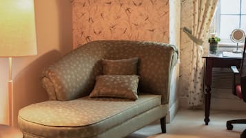A room with a curved sofa, a small table, a lamp, a mirror, and a window with curtains.