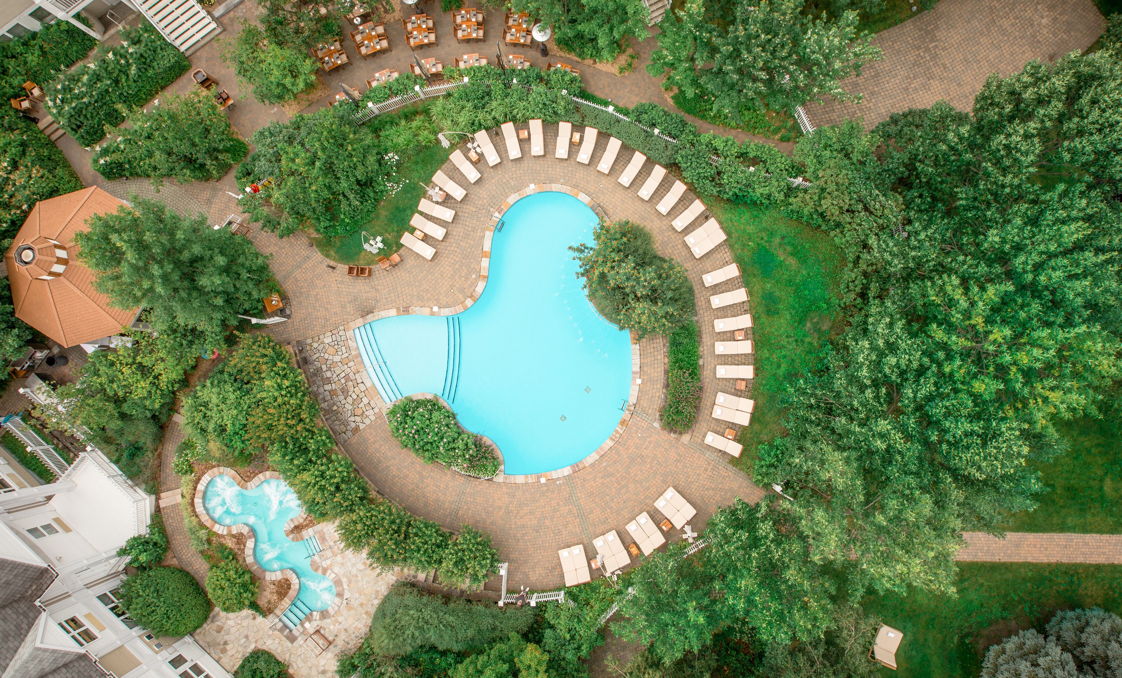 Luchtbeeld van een resort met een groot centraal zwembad, een kleiner zwembad en diverse buitenlounges, omgeven door weelderige begroeiing.