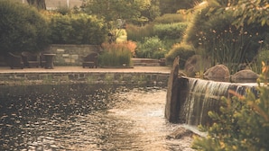 A serene outdoor area with a small waterfall, stone benches, and lush greenery. - Hotel Le Bonne Entente (Québec City)
