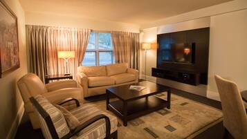 A living room with a sofa, armchairs, a coffee table, a flat-screen TV, and a lamp.