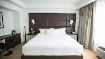 Habitación de hotel con una cama grande, cabecera oscura, dos lámparas de noche, un escritorio con silla y una ventana con cortinas.
