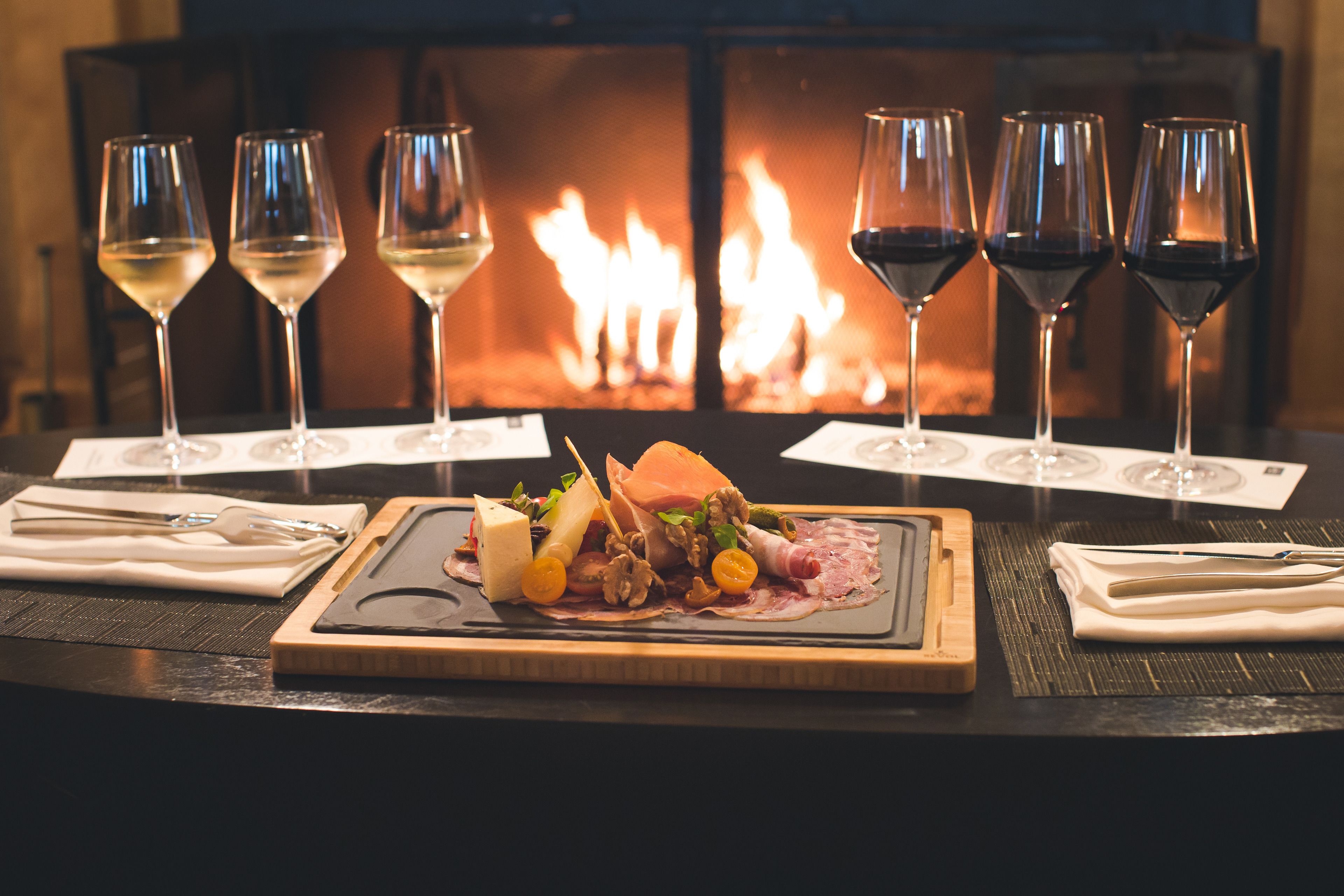 A table with a charcuterie board and wine glasses in front of a fireplace.