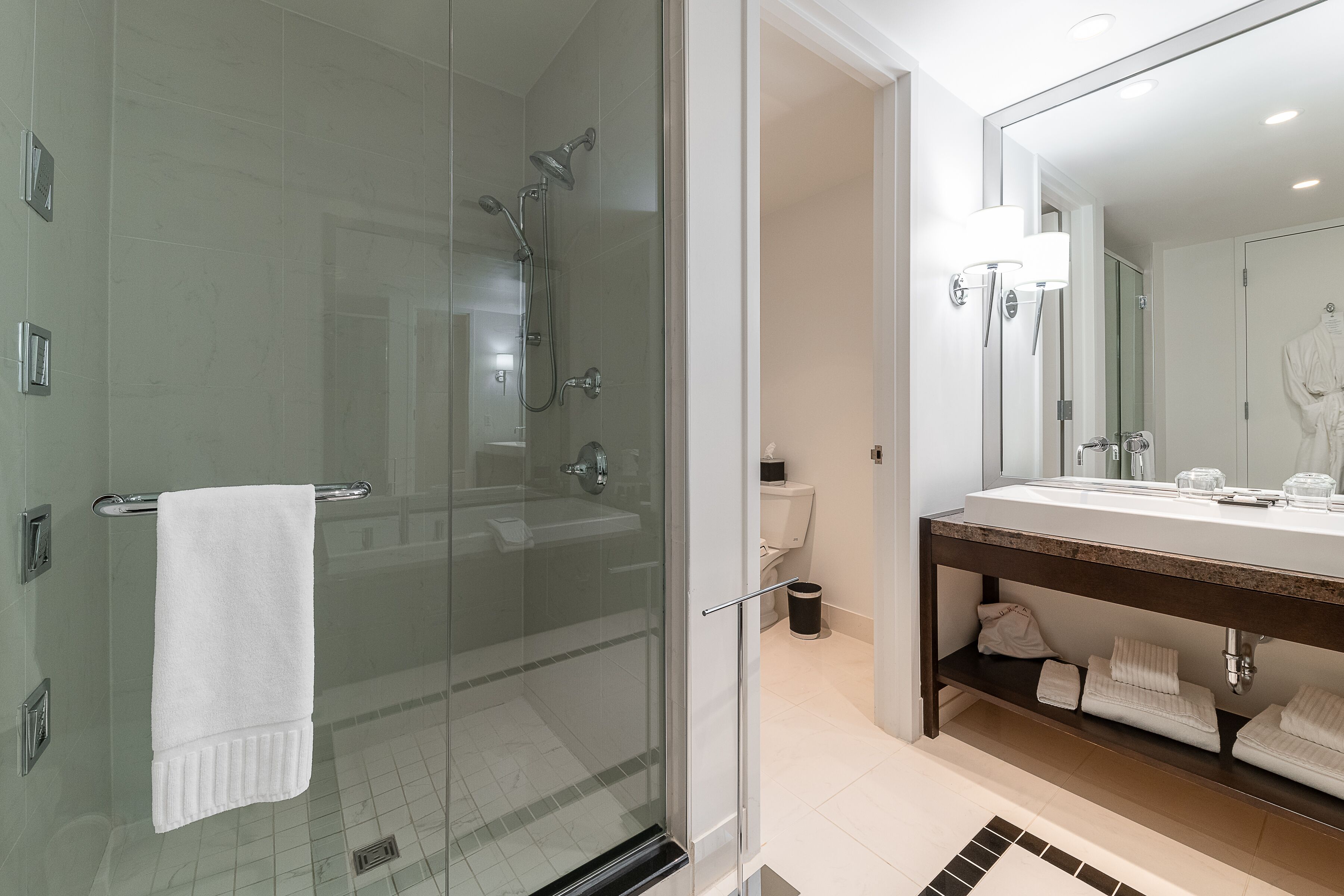 A modern bathroom with a glass-enclosed shower, a large mirror, and a vanity with a sink and towel rack.