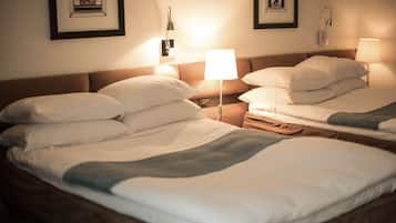 Habitación de hotel con dos camas, cada una con ropa de cama y almohadas blancas. Hay lámparas de pared a cada lado de las camas.