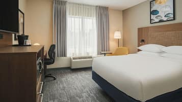 Une chambre d’hôtel équipée d’un lit, d’un bureau, d’une chaise, d’une télévision, d’une lampe et d’une fenêtre avec des rideaux.