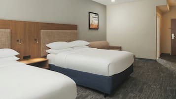A hotel room with two beds, a wooden headboard, a nightstand, and a framed picture on the wall.