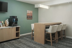 Una habitación con kitchenette, una zona de bar con taburetes, un televisor de pantalla plana en la pared y un cuadro en la pared.