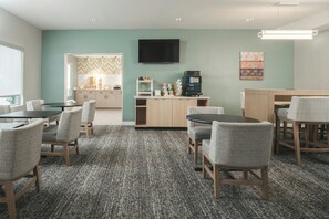 A hotel room with a kitchenette, a flat-screen TV, and a seating area with chairs and a table.