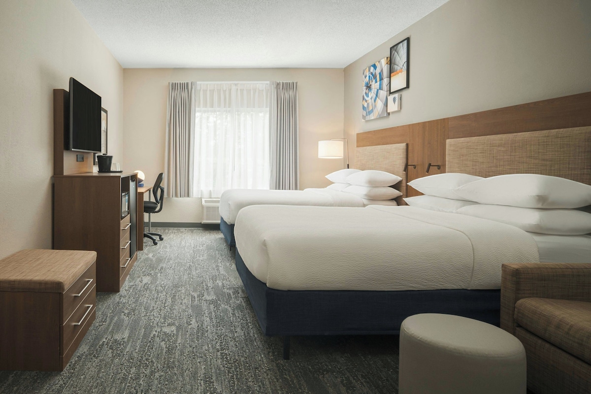 A hotel room with a large bed, a desk with a computer, a TV, and a window with curtains.