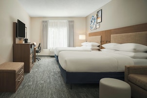 Habitación de hotel con una cama grande, un escritorio con computadora, televisor y ventana con cortinas.