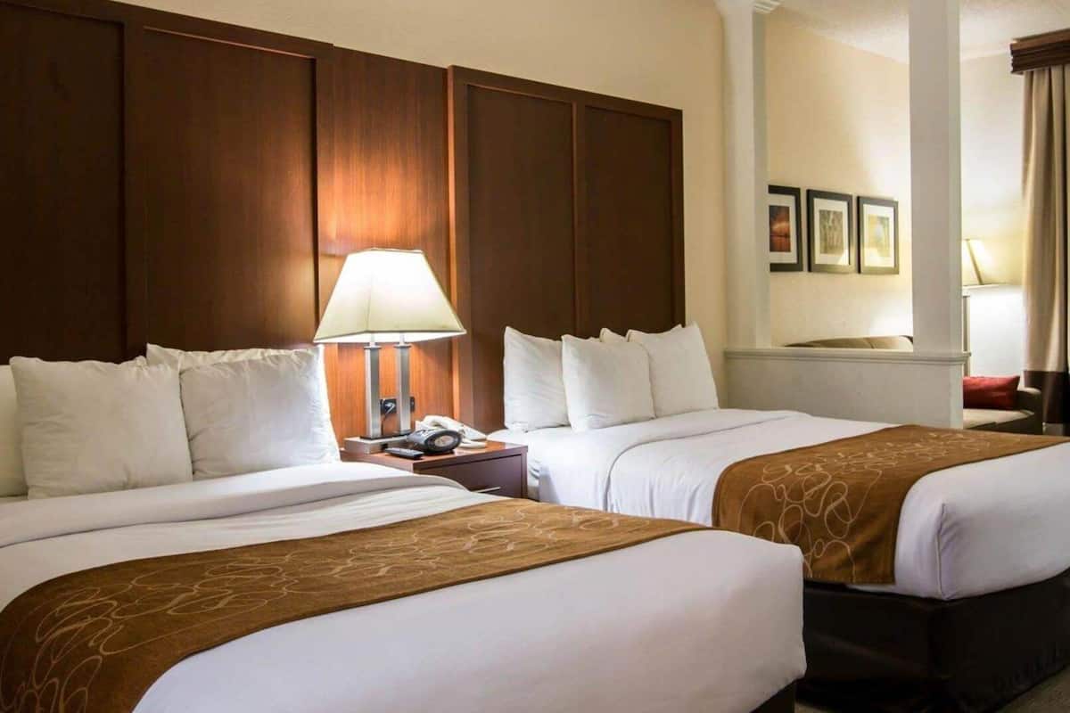 Una habitación de hotel con dos camas, un cabecero de madera, una mesita de noche con lámpara y una pequeña mesa con teléfono.