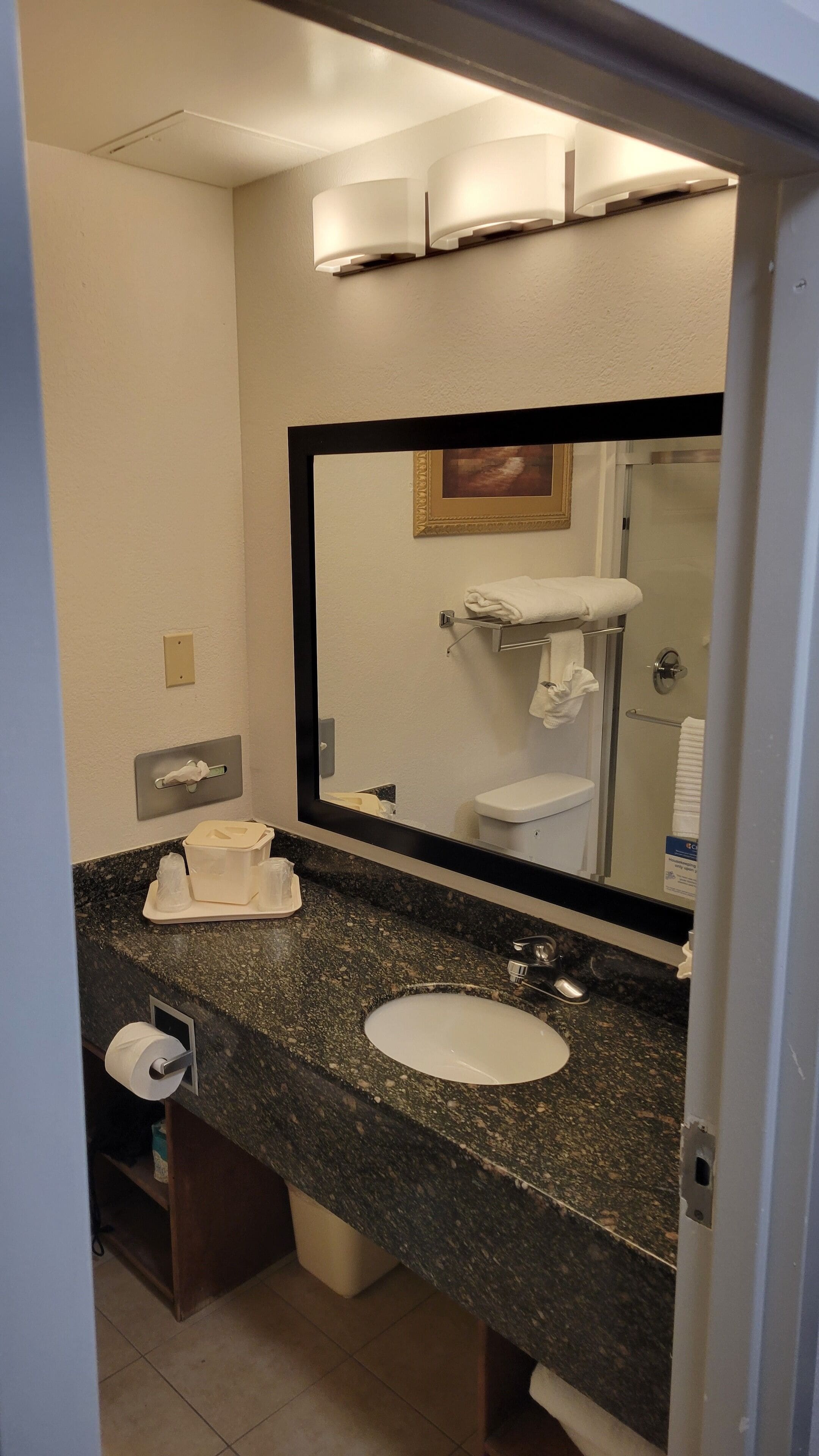 A bathroom with a granite countertop, a white sink, a mirror, a towel rack, and a toilet.