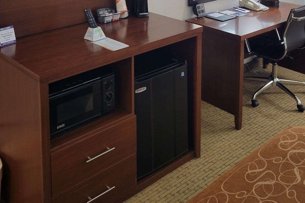 Habitación de hotel con televisión de pantalla plana, escritorio con cafetera, refrigerador, espejo y lámpara.