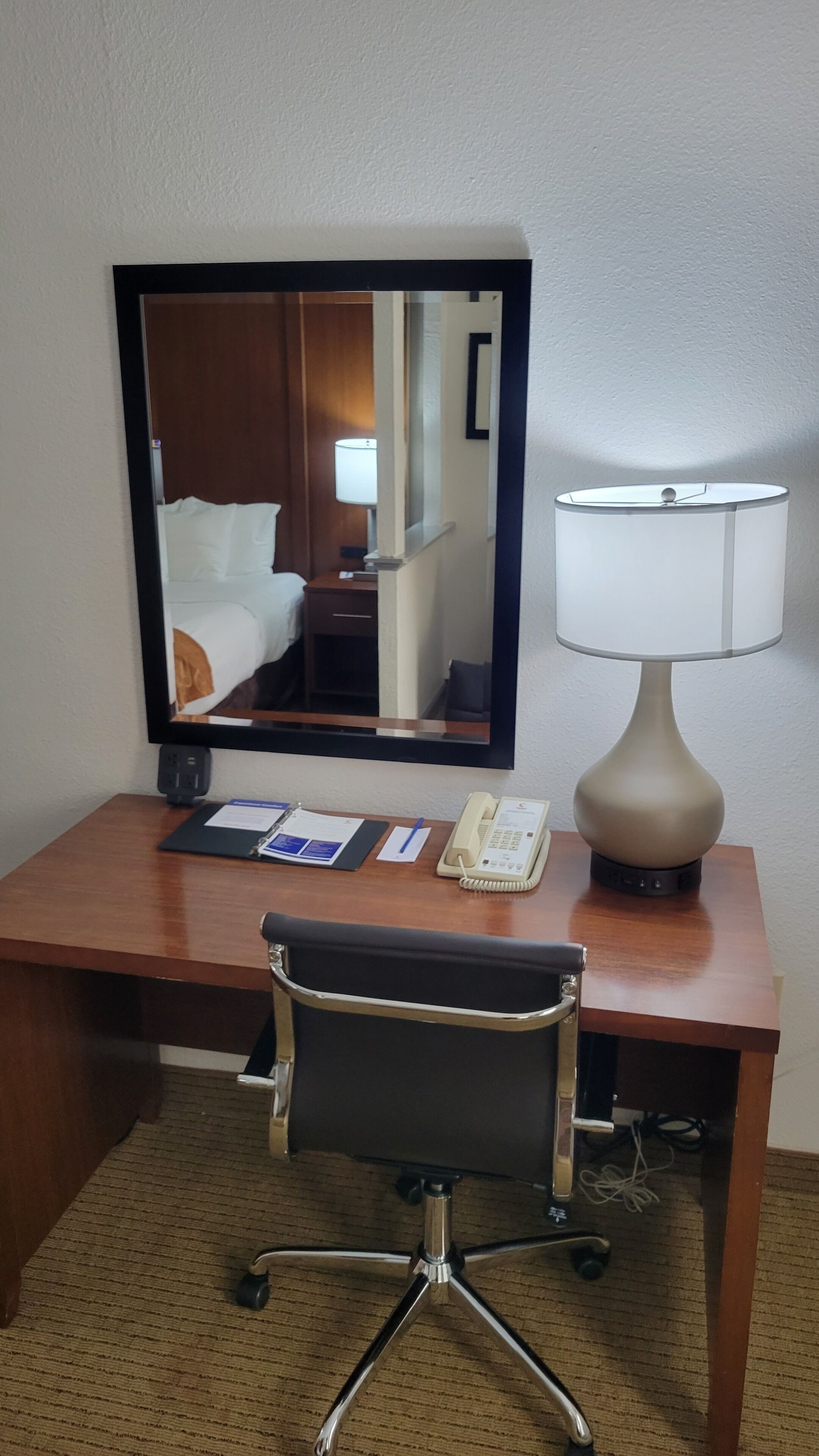 A hotel room desk with a flat-screen TV, a lamp, a telephone, and a chair.