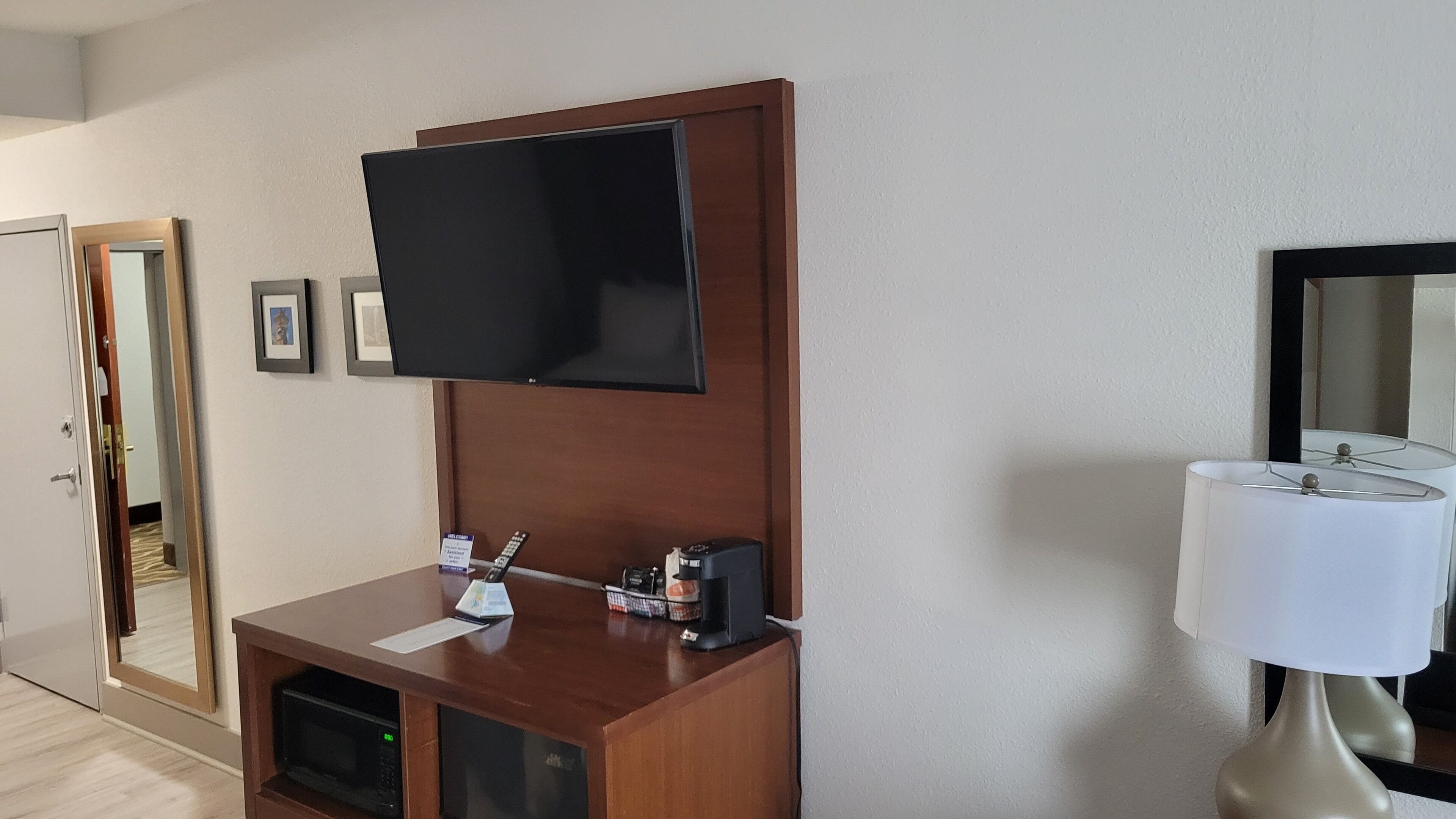 Ein Hotelzimmer mit einem Holztisch, einem flachbildfernseher an der Wand, einer Mikrowelle und einer Lampe.